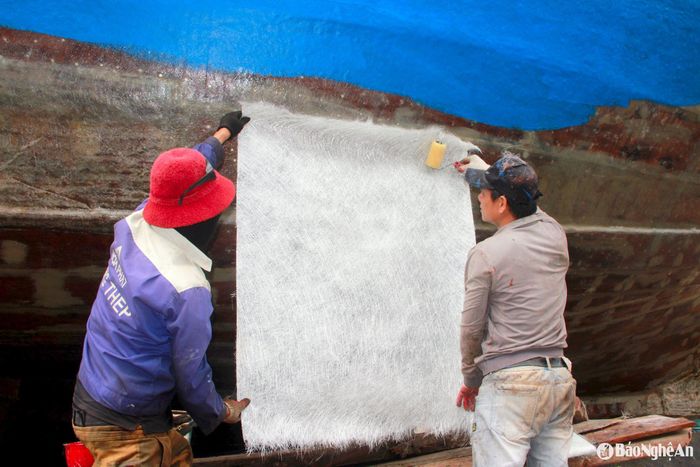 Để tăng độ chống nước cho vỏ tàu, công nhân sử dụng lưới nhựa phủ lên bề mặt, sau đó phủ thêm lớp keo dính chắc, mới tiến hành phun sơn. Ảnh: Xuân Hoàng