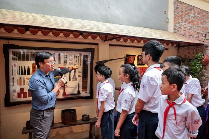 Giám tuyển Nguyễn Thế Sơn giới thiệu triển lãm “Sắc son” tại đình Hà Vĩ cho các em học sinh. Ảnh: NVCC
