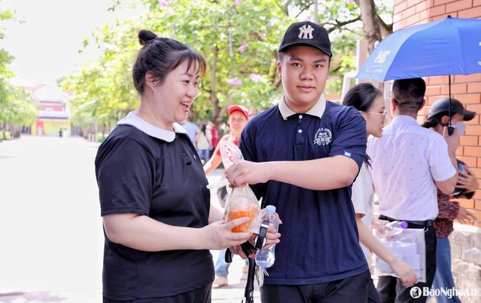 Một phụ huynh chuẩn bị sẵn nước ép trái cây mát lạnh để đưa ngay cho con khi ra khỏi phòng thi. Có người tranh thủ che mũ cho con, lau mồ hôi cho con như xua đi cái nóng mùa hè gay gắt. Ảnh: Đức Anh