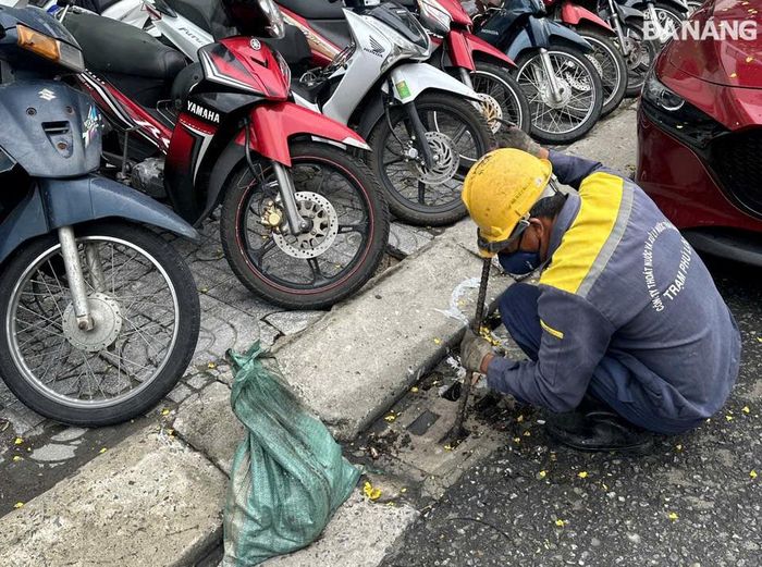 Công nhân Công ty Thoát nước và xử lý nước thải Đà Nẵng tranh thủ khơi thông cửa thu nước mưa vào chiều 11-6. Ảnh: HOÀNG HIỆP