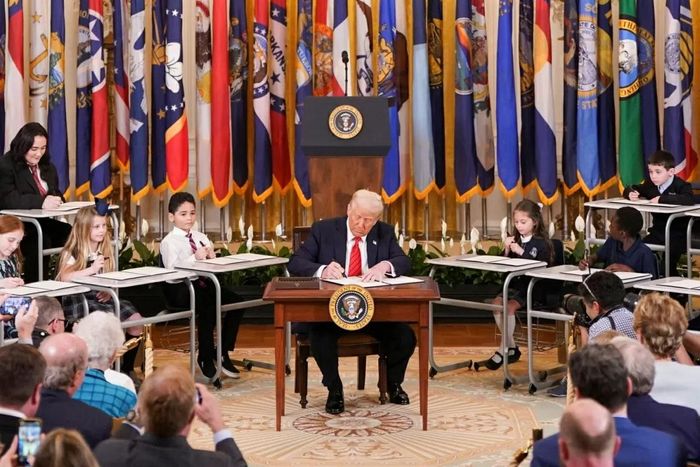 Tổng thống Mỹ Donald Trump ký sắc lệnh hành pháp tiến tới giải thể Bộ Giáo dục trong khi các em học sinh ngồi xung quanh tại Nhà Trắng, Washington, ngày 20/3/2025. (Nguồn: White House)