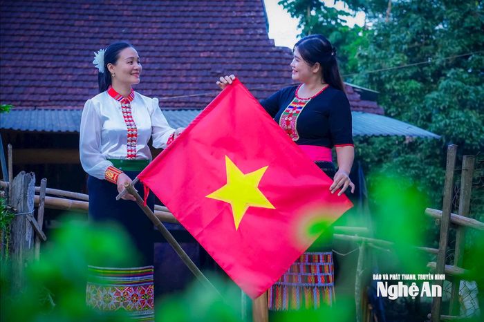Chị em người dân Thái ở xã Hùng Chân chụp ảnh cùng Quốc kỳ trong ngày lễ trọng. Ảnh: Đình Tuyên