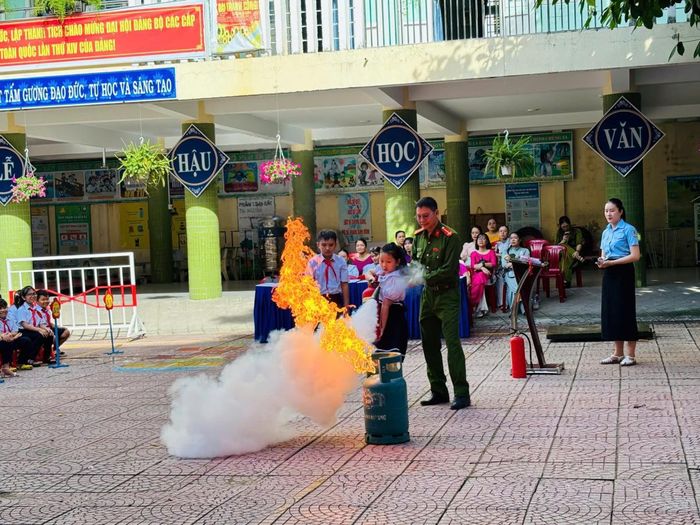 Học sinh tiểu học được cán bộ tuyên truyền hướng dẫn thực hành dùng bình chữa cháy dập tắt đám cháy giả định.