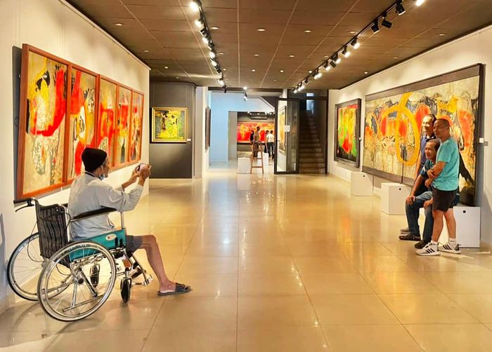 Dù đi xe lăn, nhưng Nguyễn Lâm vẫn đi xem triển lãm và chụp hình cho các con của mình. Hội Mỹ thuật TP.HCM ngày 3/12/2023. Ảnh: LĐ