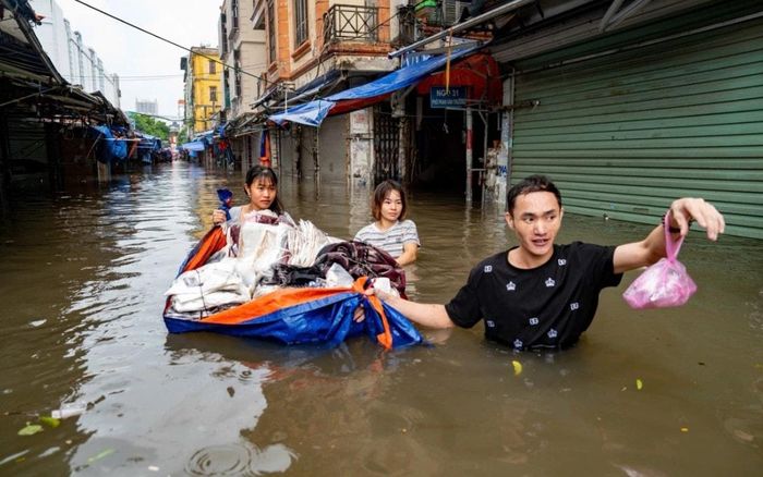 Nhóm tiểu thương dùng bạt làm "thuyền" vận chuyển hàng hóa trong nước ngập. Ảnh: Tùng Đinh