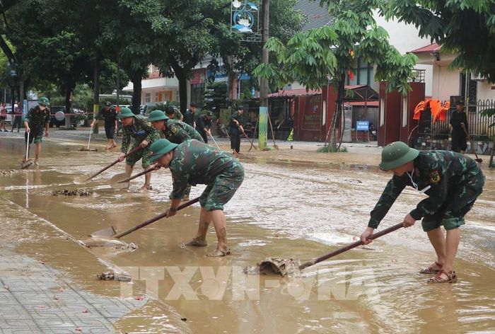 Lực lượng chức năng dọn dẹp bùn đất tại những đoạn đường phố nước đã rút. Ảnh: Chu Hiệu-TTXVN