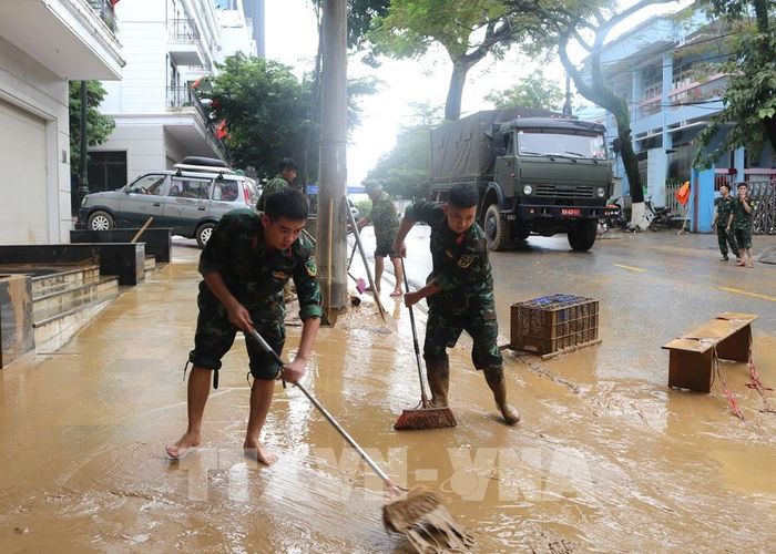 Lực lượng chức năng dọn dẹp bùn đất những đoạn đường phố nước đã rút. Ảnh: Chu Hiệu-TTXVN