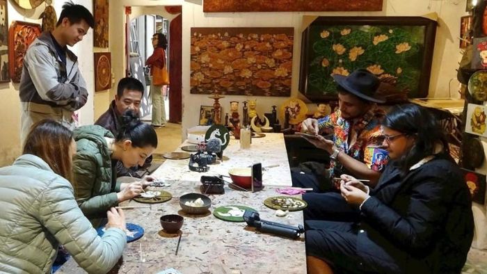 Du khách nước ngoài trải nghiệm làm sơn mài ở làng Hạ Thái. (Ảnh: LÊ BÍCH)