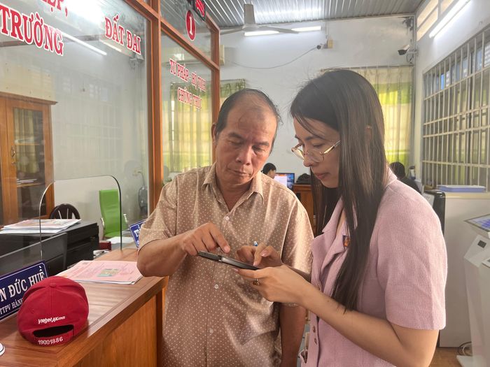 Công chức Trung tâm Hành chính công xã Nghĩa Thành (TPHCM) hướng dẫn người dân giải quyết thủ tục hành chính trực tuyến trên điện thoại. Ảnh: TRÚC GIANG