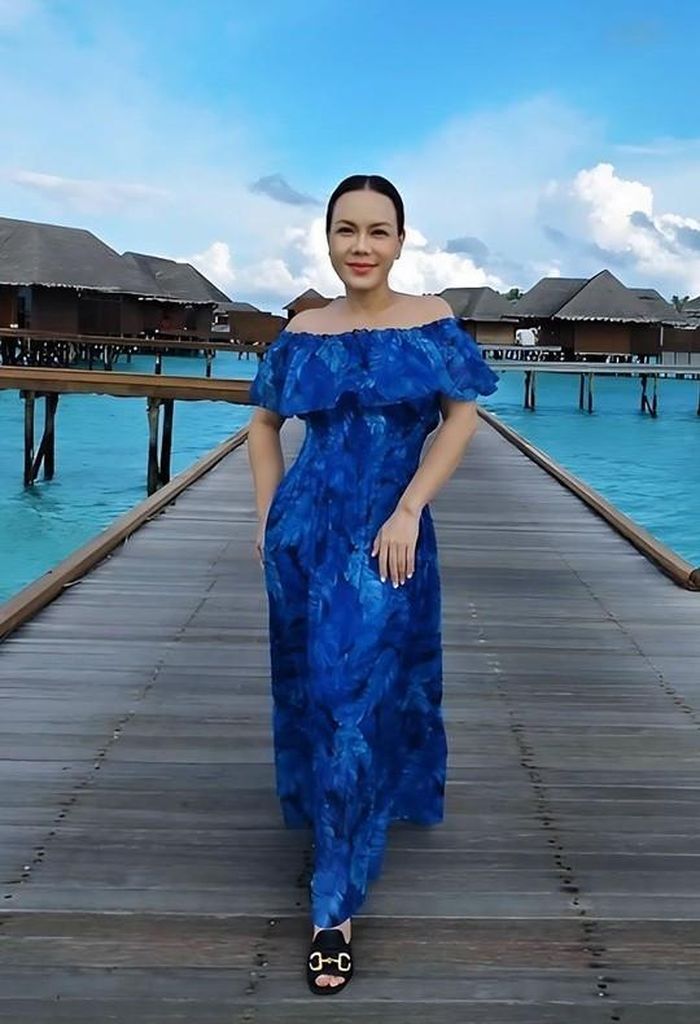 Việt Hương thường ưu tiên cách phối đồ tập trung vào váy off-shoulder để tôn tối đa phần vai thon và xương quai xanh. Cô ưa chuộng những chiếc váy chiết eo nhẹ nhàng, quyến rũ như váy maxi trễ vai dài chấm gối hoặc midi xếp ly làm lớp chính, kết hợp lớp bèo nhún hoặc voan mỏng ở phần vai để tạo độ bồng bềnh tự nhiên. Ảnh: FBNV