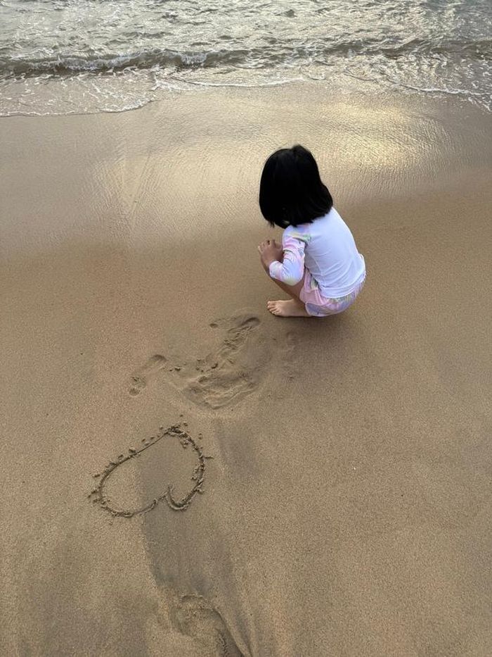 T.L vẽ hình trái tim trên cát khi đi chơi cùng mẹ. Ảnh: Gia đình cung cấp