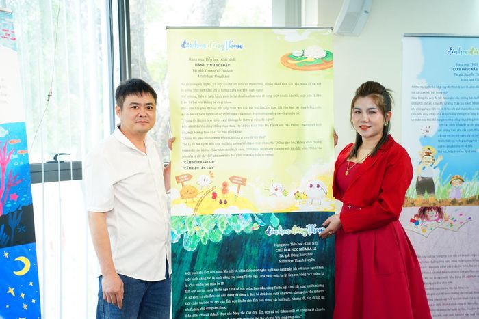 Bố mẹ của hai em Hà Nhi, Hà Anh chụp ảnh kỷ niệm bên poster tác phẩm "Hành tinh xôi đậu" - Giải Nhất hạng mục Tiểu học cuộc thi viết "Đóa hoa đồng thoại 2025". Ảnh: BTC