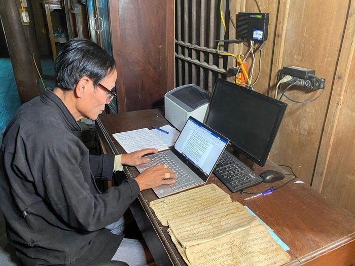 Nghệ nhân Vi Ngọc Chân đang soạn giáo án dạy chữ Thái. Ảnh: Hiền Lương