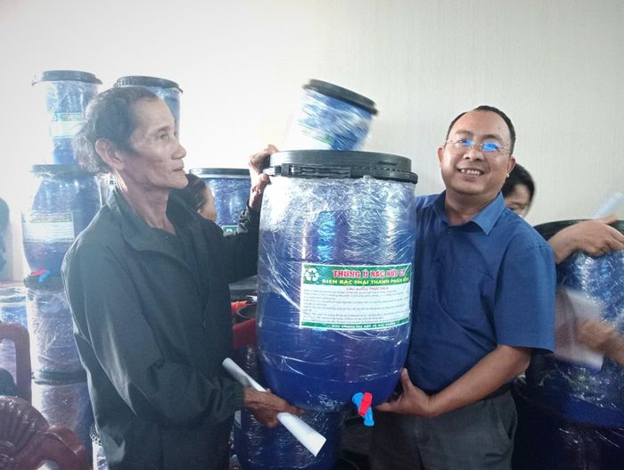Trung tâm Cung ứng dịch vụ sự nghiệp công xã Quế Sơn Trung trao thùng ủ rác hữu cơ biến rác thải thành phân bón kèm men vi sinh cho người dân. Ảnh: DUY THÁI