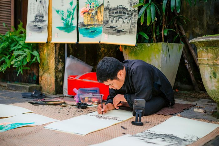 Nghệ nhân tỉ mỉ vẽ tranh thủy mặc giữa không gian xanh mát tại phố cổ Hội An.