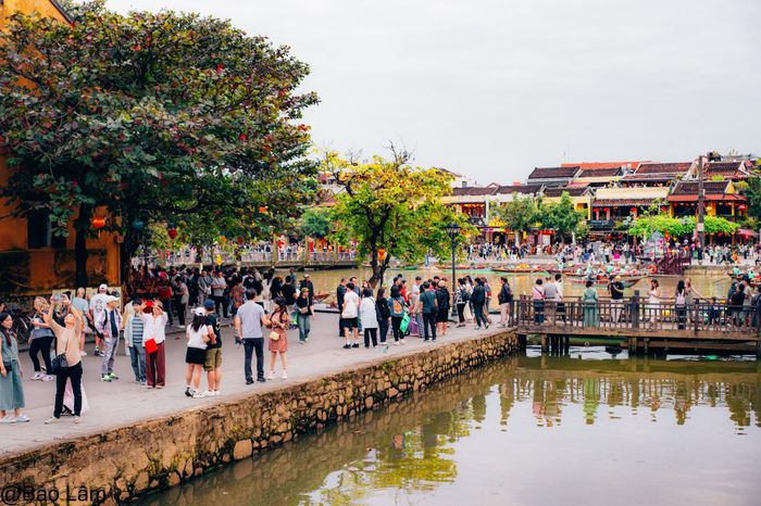 Khung cảnh nhộn nhịp bên dòng sông Hoài ở phố cổ Hội An. Du khách tản bộ ngắm cảnh, chụp ảnh và tận hưởng không gian cổ kính.