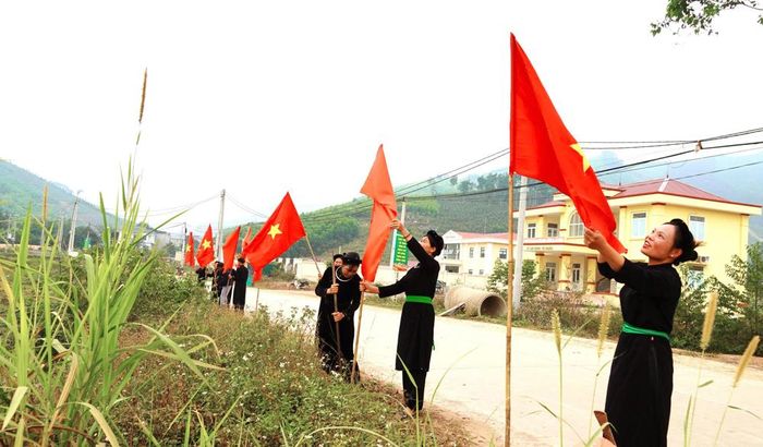  Người dân bản Nà Ó, xã An Lạc trang trí cờ dọc tuyến đường thôn. (ảnh: Xuân Thỏa) 