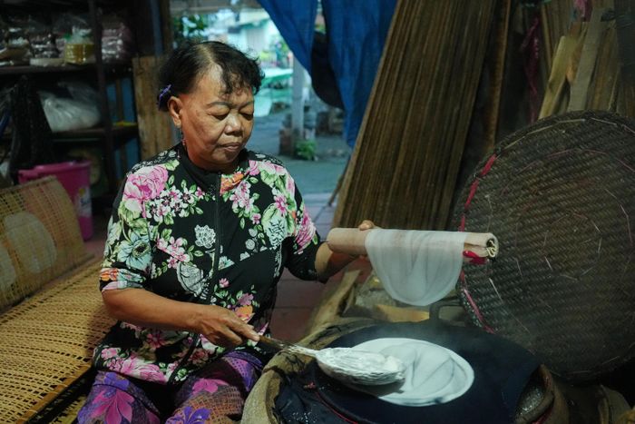  Thợ dùng gáo dừa để múc hỗn hợp bột gạo lỏng đổ lên một tấm vải phủ căng xung quanh miệng nồi. 