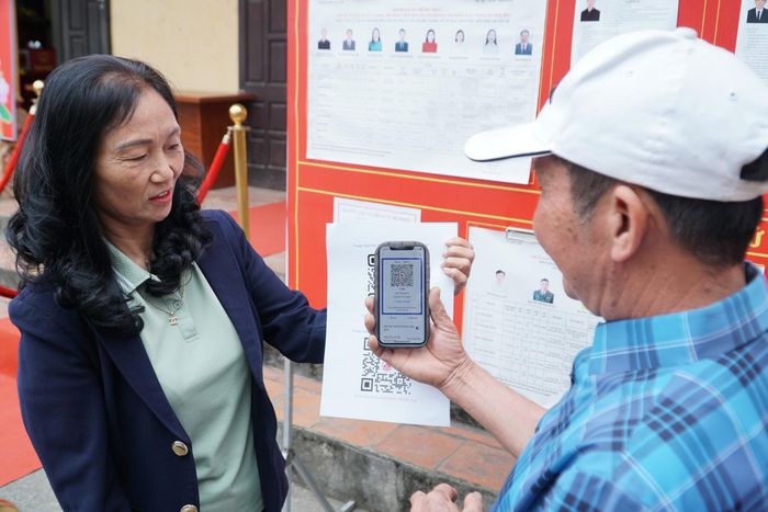 Người dân được thành viên tổ bầu cử tại khu vực bỏ phiếu số 31 hướng dẫn quét mã QR để tra cứu thông tin. Ảnh: Minh Khiêm