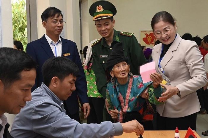 Cụ Trá Thị Dềnh vui vẻ trò chuyện với cán bộ, cử tri tại điểm bỏ phiếu.