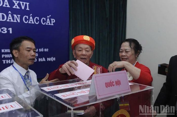 Ghi nhận tại khu vực bỏ phiếu số 02, phường Nghĩa Đô, cụ ông mặc áo dài đỏ chậm rãi bước vào buồng phiếu dưới sự hỗ trợ của lực lượng phục vụ bầu cử để lại nhiều xúc động cho những người có mặt.