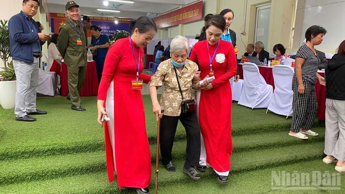 Lực lượng phục vụ bầu cử dìu cử tri cao tuổi di chuyển sau khi hoàn thành việc bỏ phiếu.
