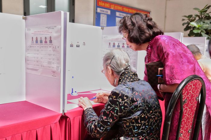 Sau khi được hướng dẫn các bước cần thiết, cụ Thuận cẩn thận nhận lá phiếu và thực hiện các thao tác theo quy định cùng với sự hỗ trợ của con gái. Dù tuổi cao, cụ vẫn giữ sự tập trung và cẩn trọng trong từng bước.