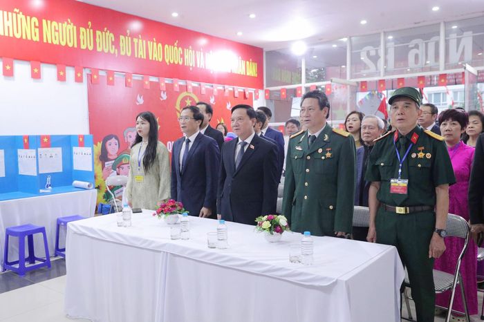Phó Chủ tịch Quốc hội Nguyễn Khắc Định và các đại biểu và cử tri thực hiện nghi thức chào cờ tại Khu vực bỏ phiếu số 16, phường Cầu Giấy, Hà Nội