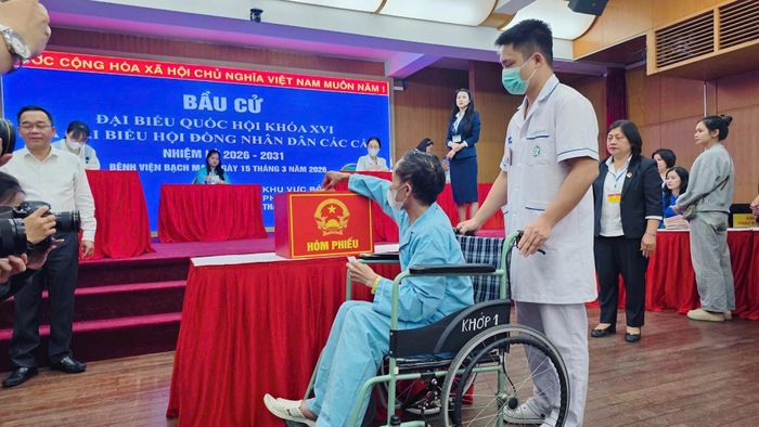 Cử tri là bệnh nhân đang điều trị tại Bệnh viện Bạch Mai được nhân viên y tế hỗ trợ di chuyển bằng xe lăn để thực hiện quyền bầu cử tại điểm bỏ phiếu lưu động - Ảnh AV