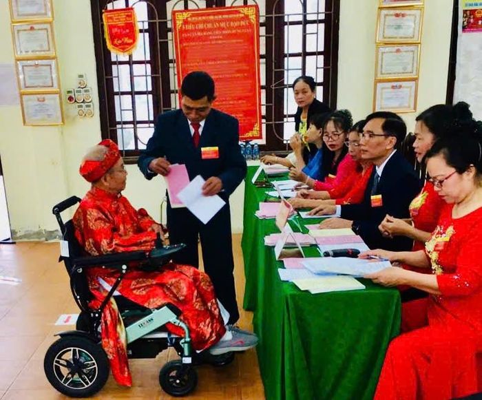 Cử tri Lê Tiến Túc, 87 tuổi, thôn Hưng Giáo, dù đau yếu, ngồi xe lăn nhưng cụ vẫn dậy từ tinh mơ, mặc áo đỏ, trực tiếp đến nhà văn hóa bỏ phiếu. Ảnh: Ánh Ngọc 