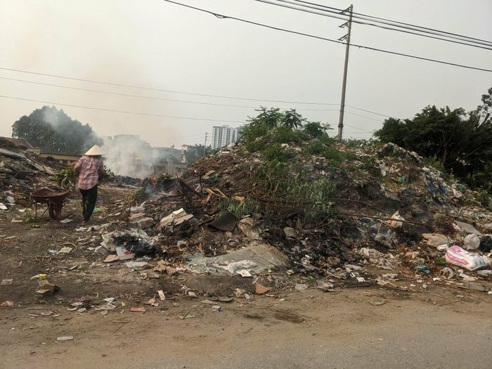 Một người phụ nữ ngang nhiên đem rác đến đổ và đốt tại một điểm vứt rác tự phát trên đường Cựu Chiến Binh, xã An Khánh (Ảnh chụp lúc 15h26 ngày 10-4-2026). Ảnh: Hồng Quý