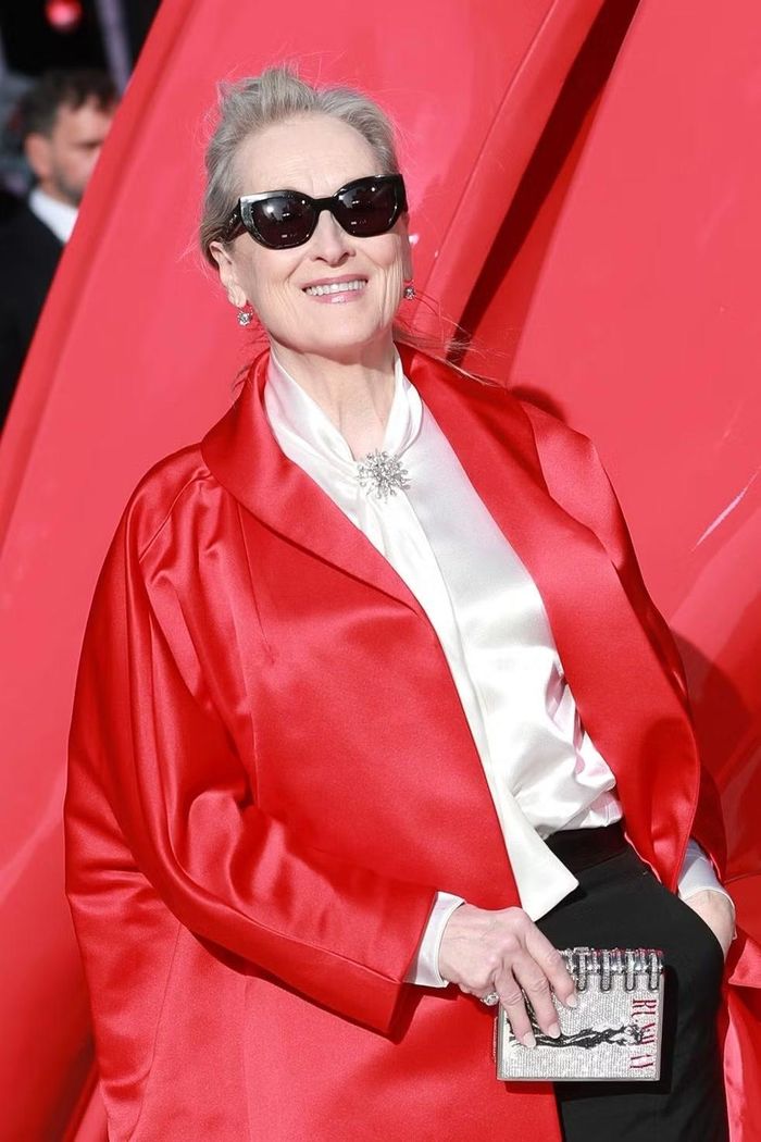 Meryl Streep chọn áo khoác satin màu đỏ của Prada, mặc bên ngoài quần đen và áo trắng có chi tiết khăn quàng cổ. Ảnh: Getty.