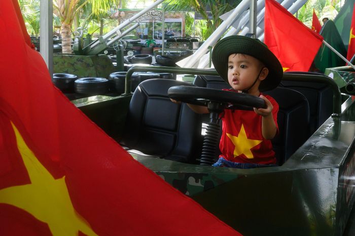  Một em nhỏ thích thú say sưa, chăm chú quan sát, cầm vô lăng xe tăng mini. Khoảnh khắc hồn nhiên giữa sắc đỏ cờ Tổ quốc mang đến cảm giác sinh động, gần gũi trong ngày lễ. 