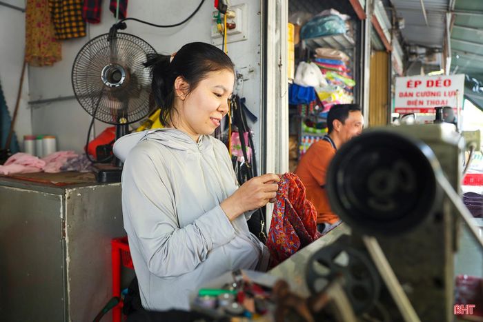 Bên trong chợ Hà Tĩnh, những ngày nghỉ lễ, chị Trần Thị Hoài vẫn tranh thủ mở quầy, ngồi bên chiếc máy may cũ, tỉ mỉ chỉnh sửa từng bộ quần áo cho khách.