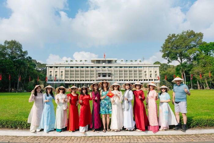 Du khách nước ngoài đội nón lá chụp hình lưu niệm tại Dinh Độc Lập.