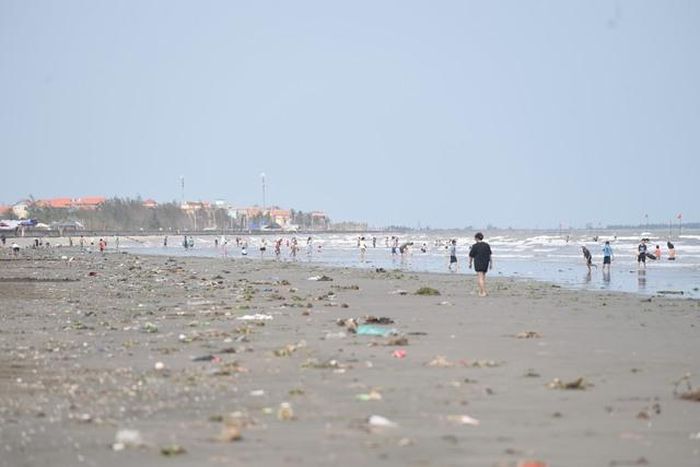 Du khách giữa bãi biển ngập rác, phía xa là những khối nhà của người dân.