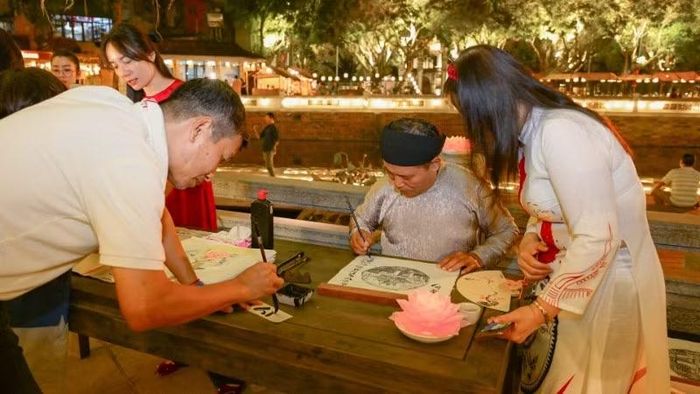 Du khách trải nghiệm viết thư pháp và xin chữ thư pháp. (Ảnh: BẢO LONG)