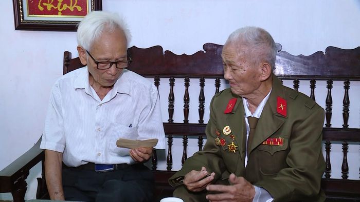 Ông Bùi Văn Đức (bên trái) và ông Phạm Văn Bướm (bên phải) cùng nhau xem lại kỷ vật là tờ giấy chứng nhận đeo huy hiệu Chiến sĩ Điện Biên Phủ.