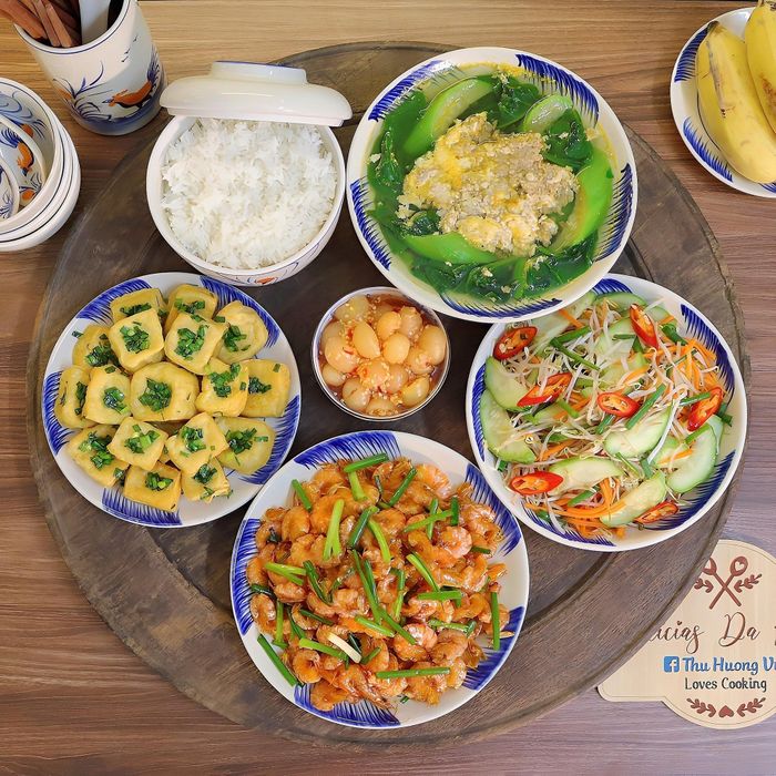 Mâm cơm có món tôm vằn biển rang, đậu phụ rán tẩm hành, canh cua nấu rau mồng tơi mướp, dưa chuột trộn giá đỗ. 