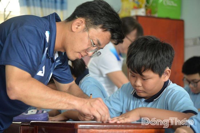 Anh Trần Nguyễn Ngọc Đức cầm tay một em nhỏ, nhẹ nhàng chỉnh lại cách cầm bút. 