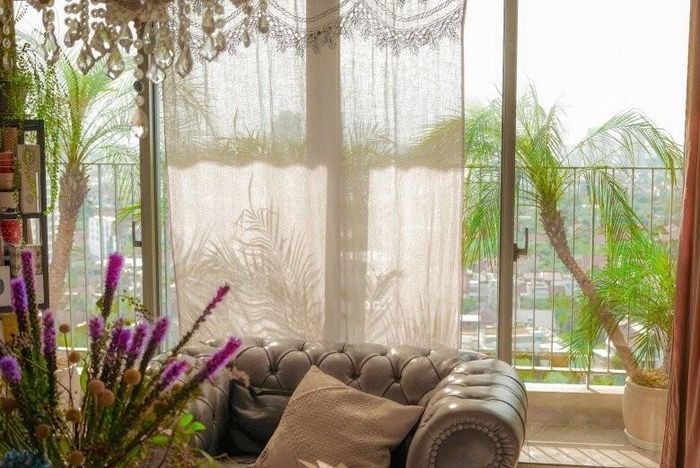 Khung cửa sổ lộng gió mở ra tầm nhìn thoáng đãng, nơi những tán cọ xanh mát mắt giao thoa cùng rèm lụa mỏng manh. Chiếc sofa da cao cấp màu trung tính tạo điểm tựa vững chãi, mang lại cảm giác thư thái tuyệt đối cho chủ nhân sau giờ làm việc.
