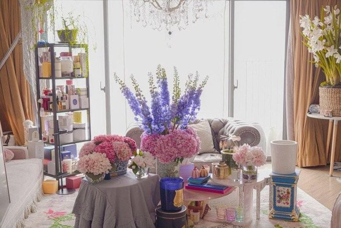 Phòng khách tràn ngập hơi thở lãng mạn với sự hiện diện của những đóa cẩm tú cầu hồng rực rỡ cùng lan hồ điệp trắng quý phái. Các kệ đồ trưng bày nến thơm và mỹ phẩm cao cấp được sắp xếp ngăn nắp, phản ánh đúng tinh thần "bị OCD nặng" nhưng đầy tính nghệ thuật của chủ nhân.