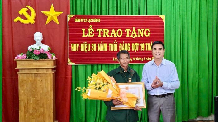 Đồng chí Đỗ Khắc Lợi, Phó Bí thư Thường trực Đảng ủy xã Lạc Dương trao tặng Huy hiệu 30 năm tuổi Đảng cho đảng viên Kơ Đơng Ha Dương