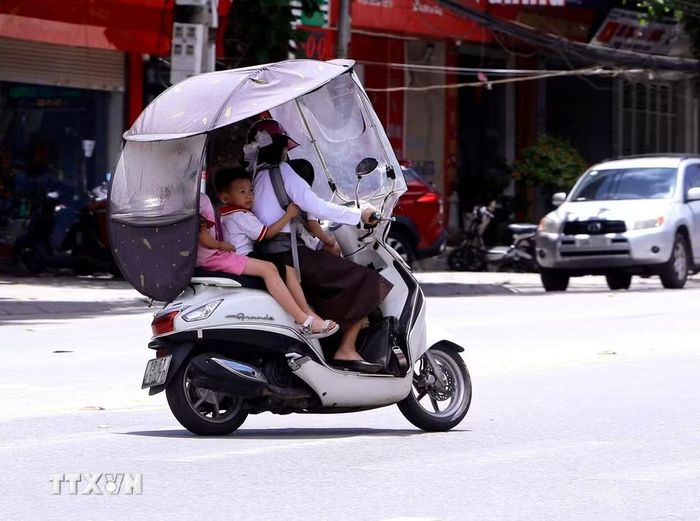 Giữa đỉnh điểm nắng nóng mùa Hè, nhiều người dân lắp thêm mái che chống nắng cho xe máy khi chở trẻ nhỏ di chuyển trên đường phố tỉnh Phú Thọ. (Ảnh: Hoàng Hùng/TTXVN)