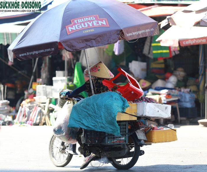 Người phụ nữ che ô, len lỏi giữa cái nắng gay gắt để bán hàng rong mưu sinh.