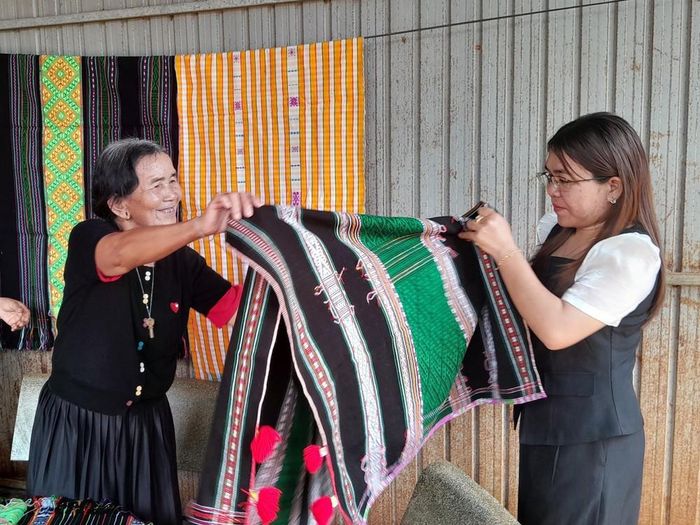 Bà Thị Y Rơ (76 tuổi, người dân tộc M’nông) giới thiệu tấm thổ cẩm đã hoàn chỉnh cho chuyên viên phòng văn hóa-xã hội xã Bù Gia Mập. Ảnh: K GƯỈH-TTXVN