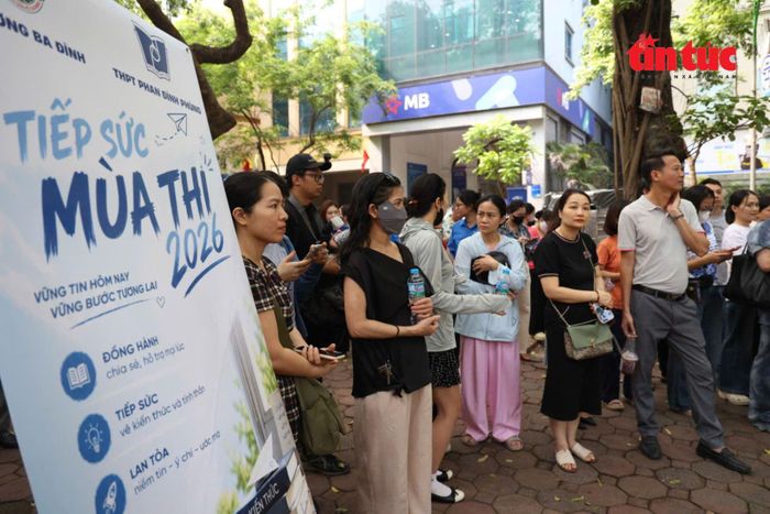 Phụ huynh chờ con bên ngoài điểm thi, cạnh bảng thông tin “Tiếp sức mùa thi 2026”.
