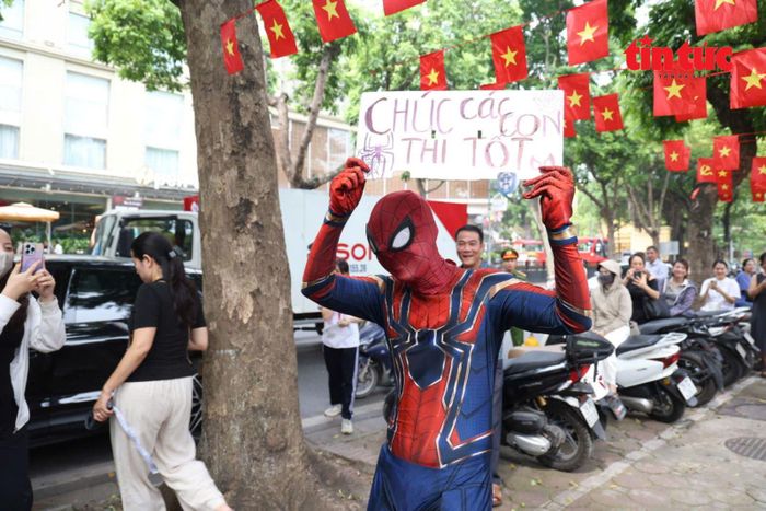 Một người mặc trang phục nhân vật Spiderman giơ cao bảng “Chúc các con thi tốt”, thu hút sự chú ý của thí sinh và phụ huynh.