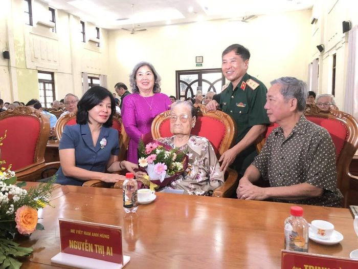 Trung tướng Trần Tấn Hùng - Phó Chủ tịch Hội HTGĐLS Việt Nam và bà Lê Thị Thu, nguyên Bộ trưởng – Chủ nhiệm Ủy ban Dân số, gia đình và trẻ em (hai người đứng) tặng hoa cho Mẹ Việt Nam Anh hùng Nguyễn Thị Ai.