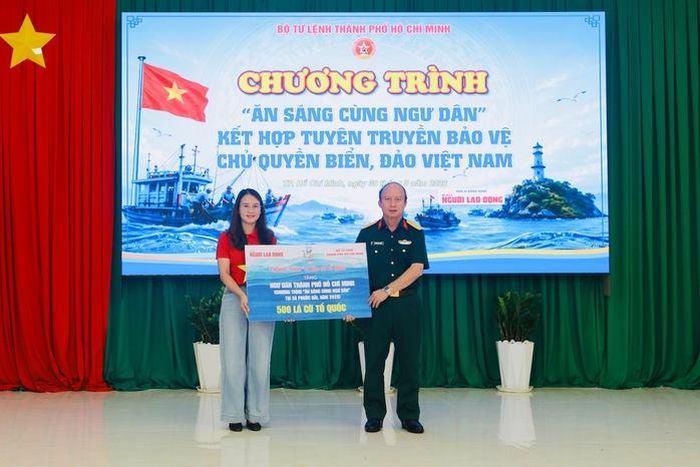 Nhà báo Hoàng Thị Bích Ngọc - Đại diện Báo Người Lao Động trao tặng bảng tượng trưng 500 lá cờ Tổ quốc đến đại tá Nguyễn Đình Chuẩn, Phó Chính ủy Bộ Tư lệnh TPHCM; ảnh: L.Trầm
